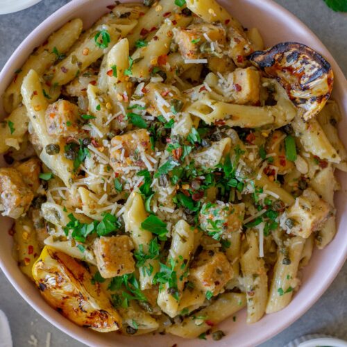 Overhead shot of one pan tofu piccata pasta topped with fresh parsley, fried capers, a sprinkle of parmesan and a grilled lemon slice.