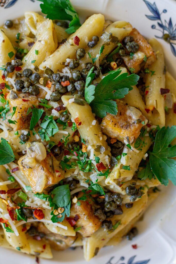 a close-up of one pan tofu piccata pasta served in a bowl and topped with vegan parmesan and fresh parsley.