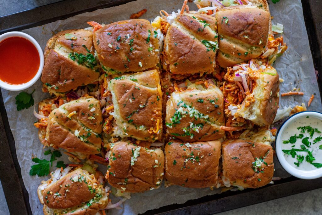 Overhead shot of buffalo tofu sliders with melty cheese, crispy golden tops, and a side of ranch and buffalo sauce for dipping.