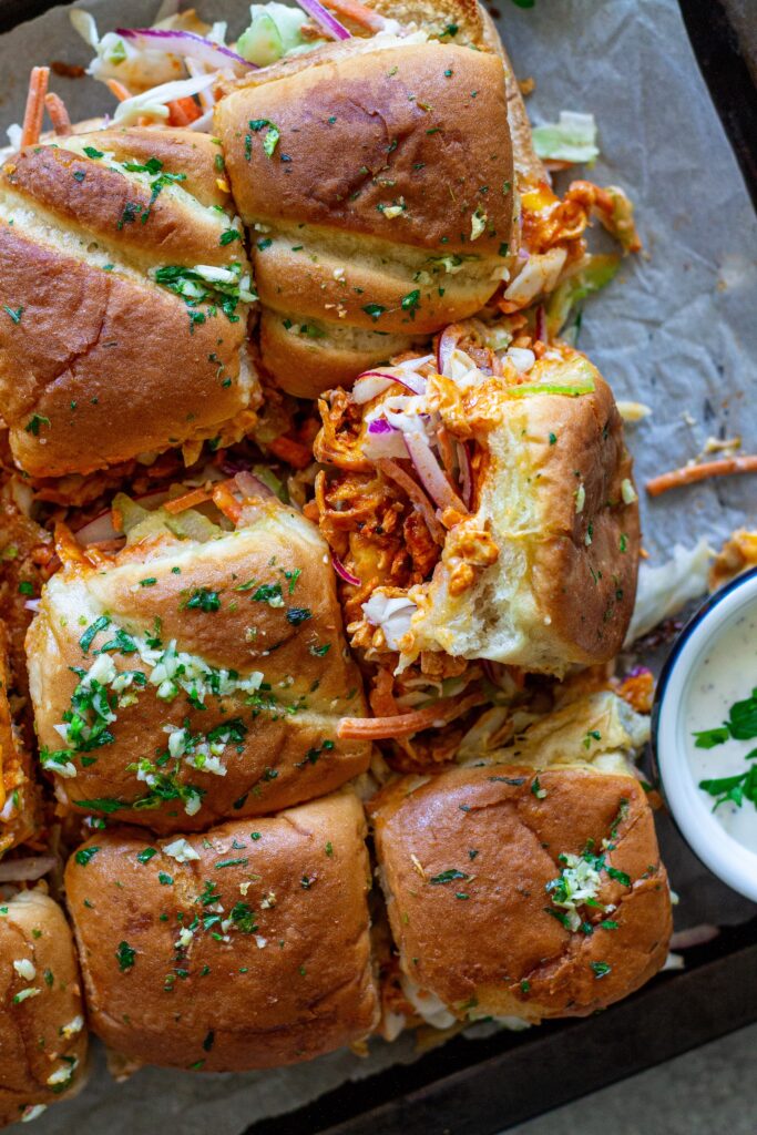 Close-up of buffalo tofu sliders with melty cheese, crispy golden tops, and a side of ranch and buffalo sauce for dipping.