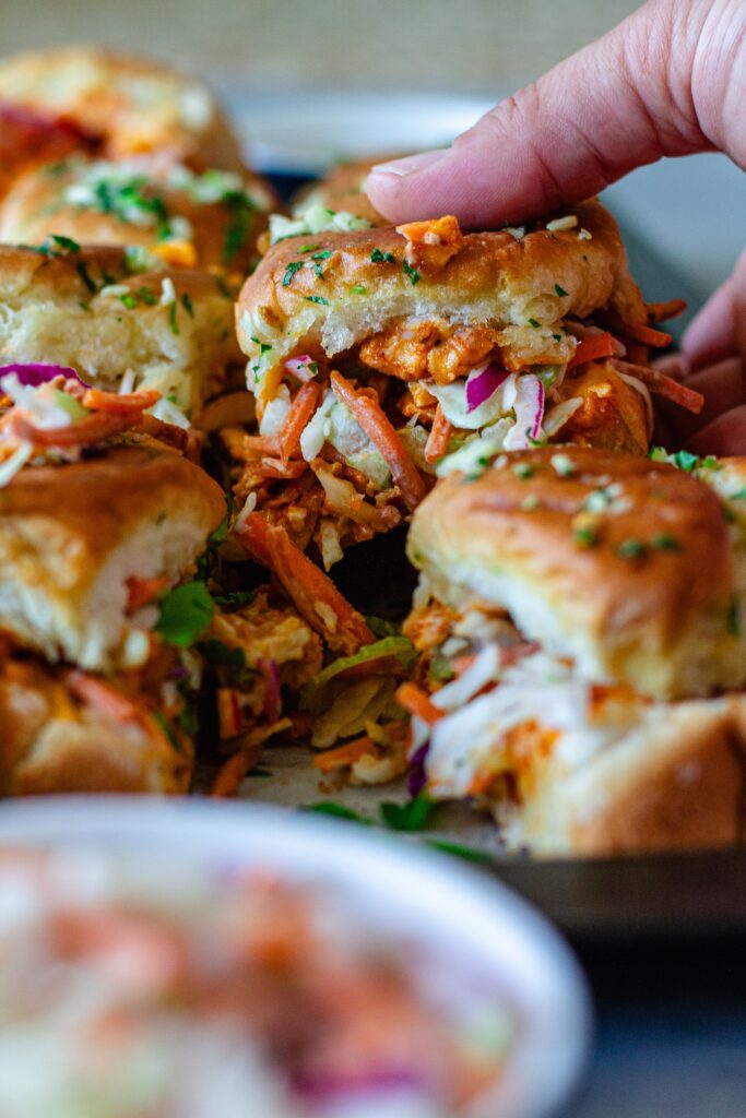Close-up of buffalo tofu sliders with melty cheese, crispy golden tops, and a side of ranch and buffalo sauce for dipping.