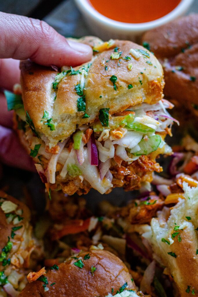 Close-up of buffalo tofu sliders with melty cheese, crispy golden tops, and a side of ranch and buffalo sauce for dipping.
