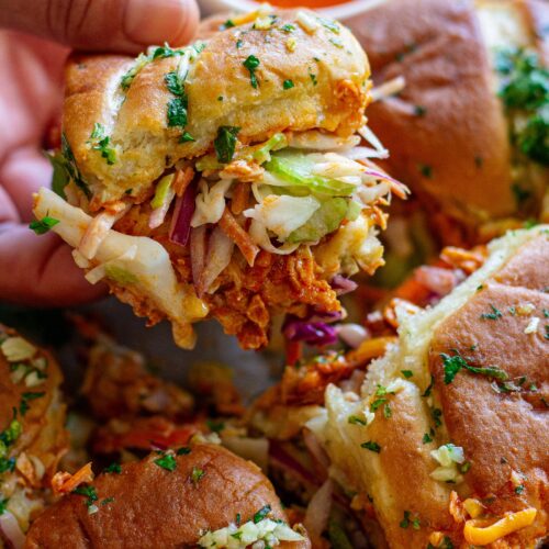 Close-up of buffalo tofu sliders with melty cheese, crispy golden tops, and a side of ranch and buffalo sauce for dipping.