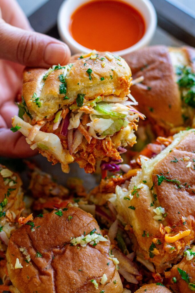 Close-up of buffalo tofu sliders with melty cheese, crispy golden tops, and a side of ranch and buffalo sauce for dipping.