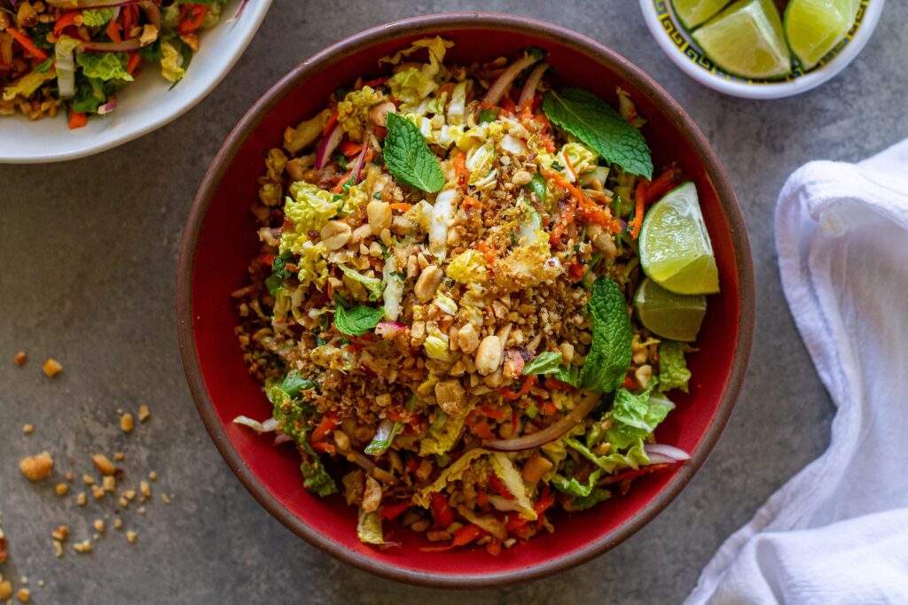 Overhead shot of vegan Vietnamese chicken salad in a serving bowl garnished with roasted peanuts, fried shallots, and fresh lime wedges.