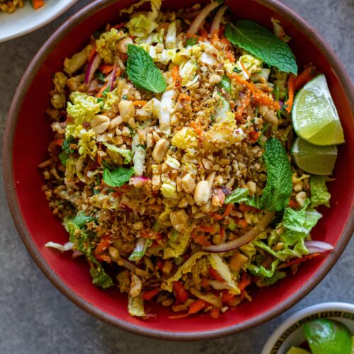 Overhead shot of vegan Vietnamese chicken salad in a serving bowl garnished with roasted peanuts, fried shallots, and fresh lime wedges.