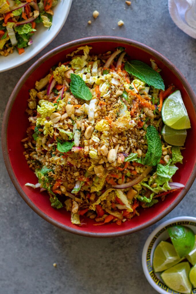 Overhead shot of vegan Vietnamese chicken salad in a serving bowl garnished with roasted peanuts, fried shallots, and fresh lime wedges.