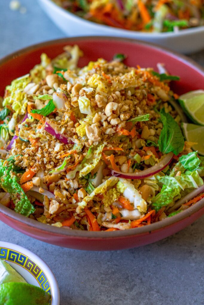 close-up of vegan Vietnamese chicken salad in a serving bowl garnished with roasted peanuts, fried shallots, and fresh lime wedges.
