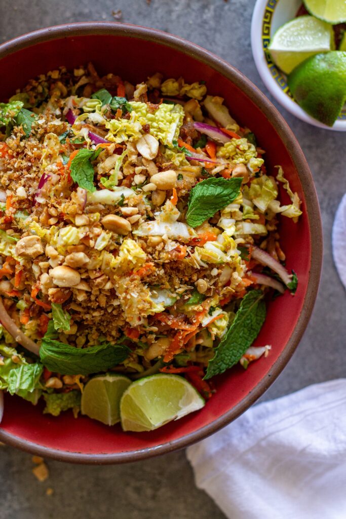 Overhead shot of vegan Vietnamese chicken salad in a serving bowl garnished with roasted peanuts, fried shallots, and fresh lime wedges.