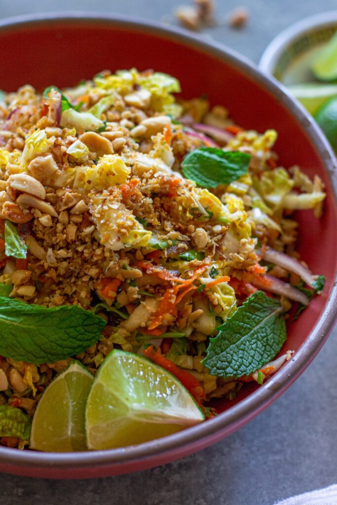 Overhead shot of vegan Vietnamese chicken salad in a serving bowl garnished with roasted peanuts, fried shallots, and fresh lime wedges.