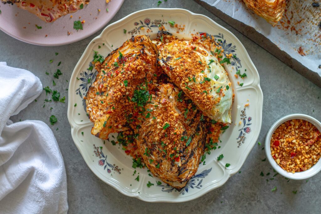 Grilled cabbage wedges topped with Calabrian chili lemon aioli, crispy golden breadcrumbs, and fresh minced parsley on a serving platter.