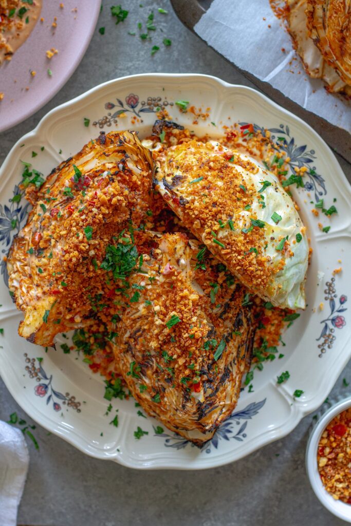 Grilled cabbage wedges topped with Calabrian chili lemon aioli, crispy golden breadcrumbs, and fresh minced parsley on a serving platter.