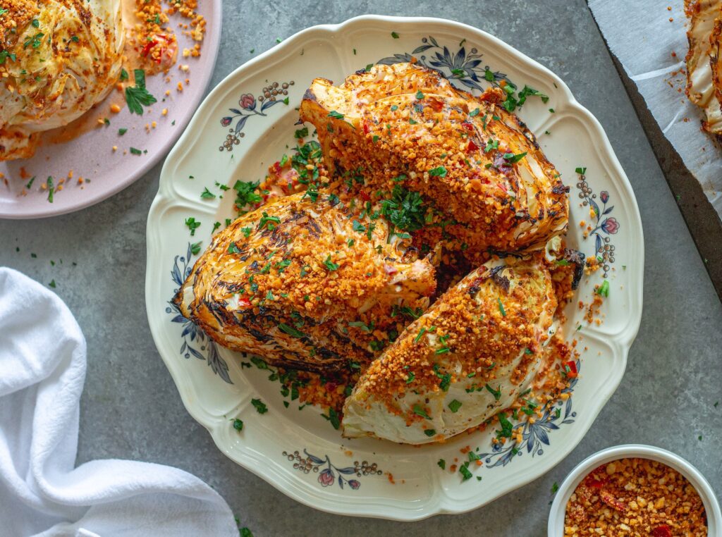 Grilled cabbage wedges topped with Calabrian chili lemon aioli, crispy golden breadcrumbs, and fresh minced parsley on a serving platter.