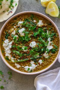 Shot of one pan coconut lentil curry garnished with coconut cream and cilantro, and served with a side of rice.