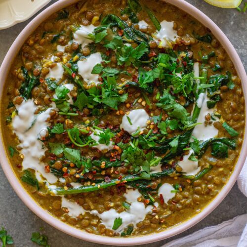 Shot of one pan coconut lentil curry garnished with coconut cream and cilantro, and served with a side of rice.