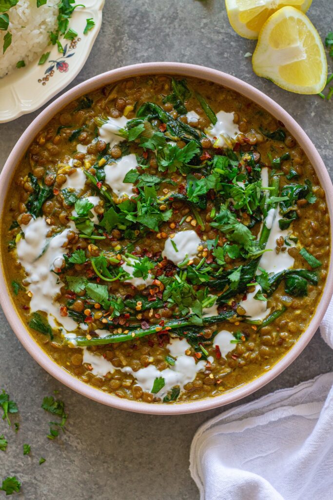Shot of one pan coconut lentil curry garnished with coconut cream and cilantro, and served with a side of rice.
