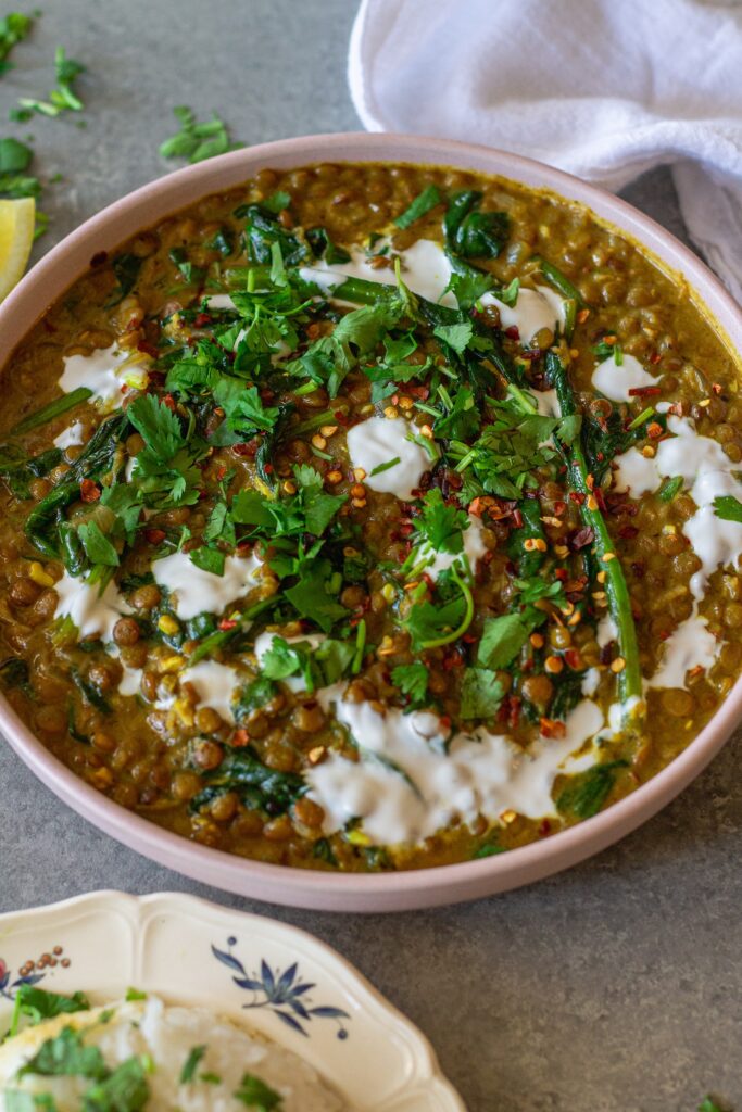 Shot of one pan coconut lentil curry garnished with coconut cream and cilantro, and served with a side of rice.