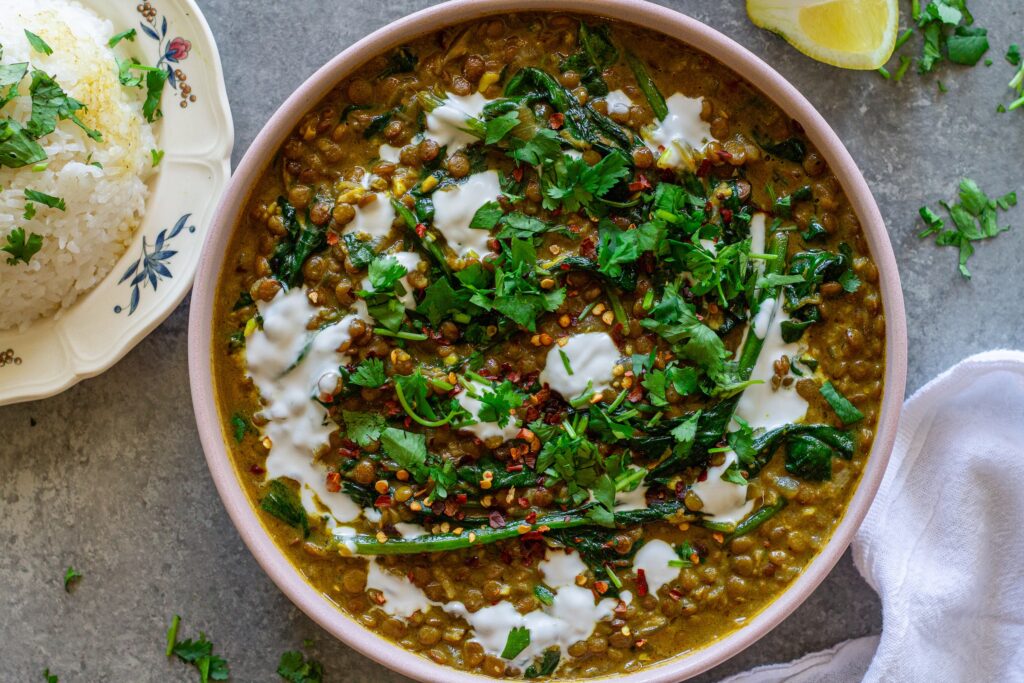 Shot of one pan coconut lentil curry garnished with coconut cream and cilantro, and served with a side of rice.