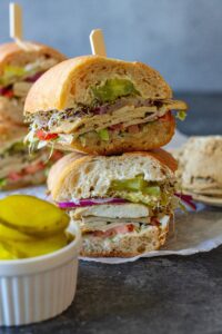 Tofu deli meat slices arranged in a sandwich with pickles, lettuce, tomato, sprouts, and onion.