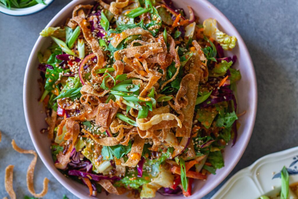 picture of vegan bang bang chicken salad on a serving plate with shredded tofu ‘chicken', colorful veggies, creamy bangs bang dressing, and crispy wontons.