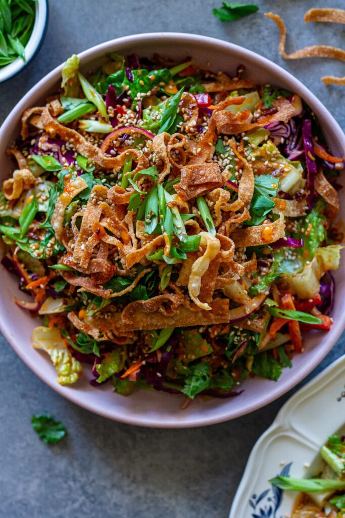 picture of vegan bang bang chicken salad on a serving plate with shredded tofu ‘chicken', colorful veggies, creamy bangs bang dressing, and crispy wontons.