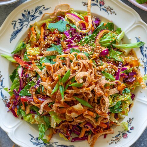 picture of vegan bang bang chicken salad on a serving plate with shredded tofu ‘chicken', colorful veggies, creamy bangs bang dressing, and crispy wontons.