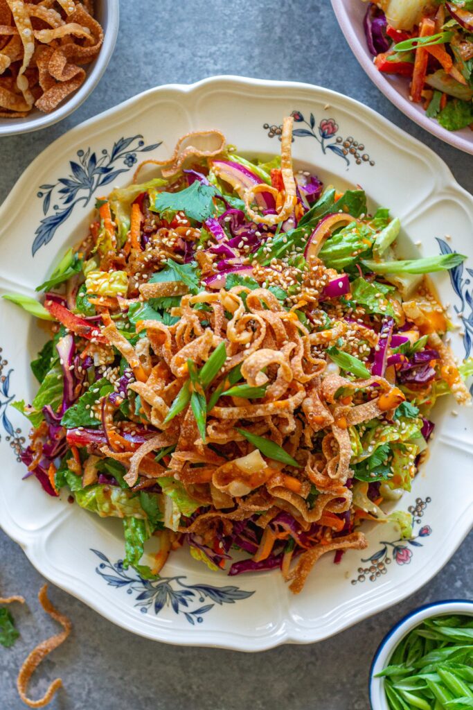picture of vegan bang bang chicken salad on a serving plate with shredded tofu ‘chicken', colorful veggies, creamy bangs bang dressing, and crispy wontons.