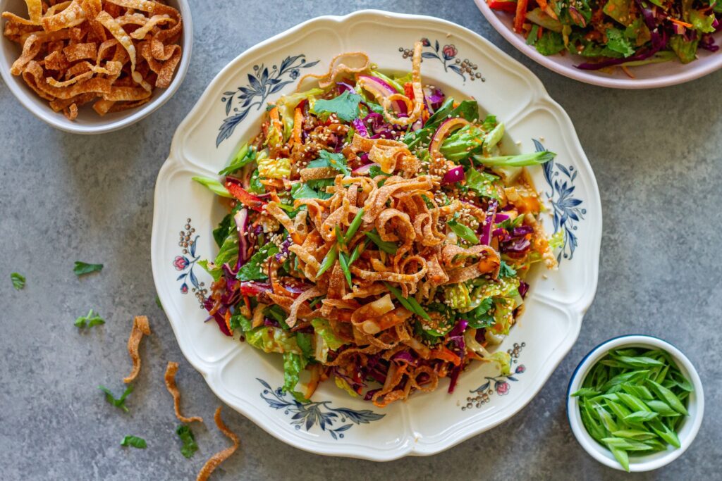 picture of vegan bang bang chicken salad on a serving plate with shredded tofu ‘chicken', colorful veggies, creamy bangs bang dressing, and crispy wontons.