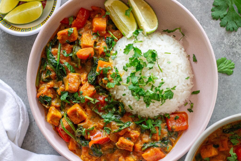 Coconut tofu and sweet potato skillet served alongside jasmine rice, and topped with fresh cilantro and a side of lime wedges.