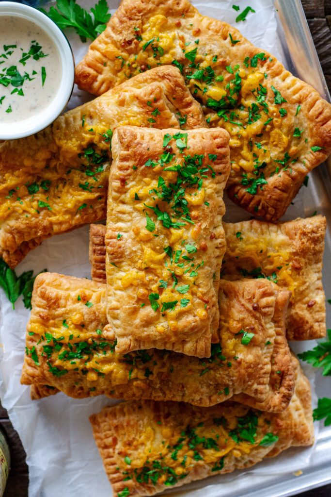 Golden brown crispy Cajun-inspired hand pies stacked on a plate with cheddar cheese and parsley garnish.