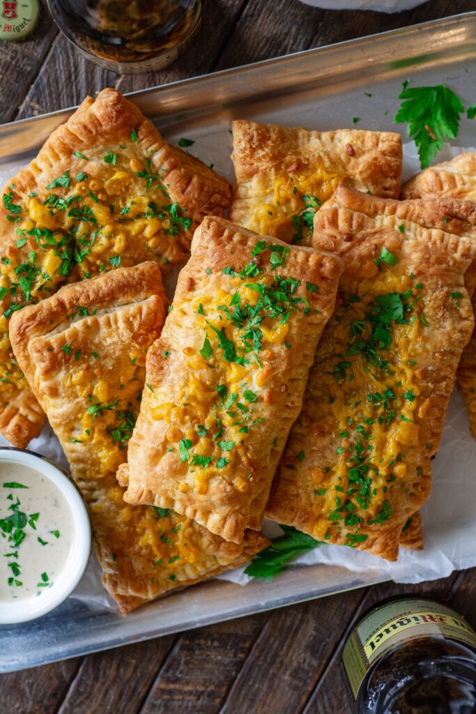 Golden brown crispy Cajun-inspired hand pies stacked on a plate with cheddar cheese and parsley garnish.