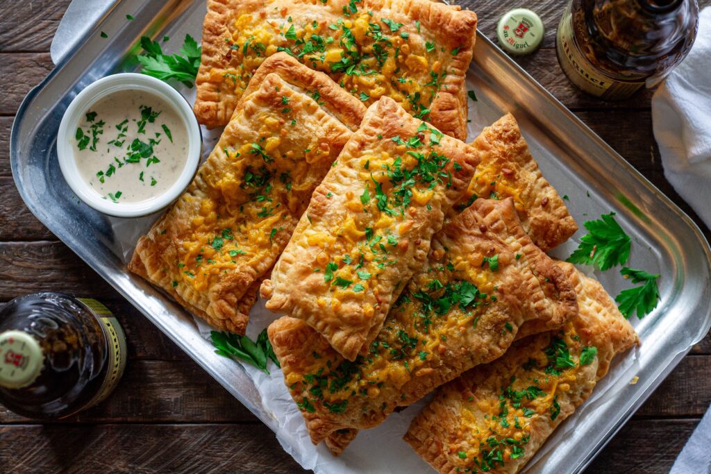 Golden brown crispy Cajun-inspired hand pies stacked on a plate with cheddar cheese and parsley garnish.