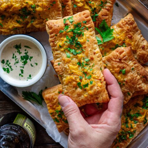 Golden brown crispy Cajun-inspired hand pies stacked on a plate with cheddar cheese and parsley garnish.