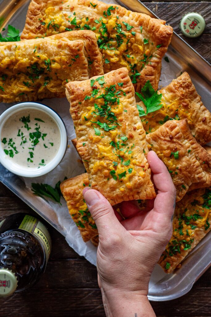 Golden brown crispy Cajun-inspired hand pies stacked on a plate with cheddar cheese and parsley garnish.