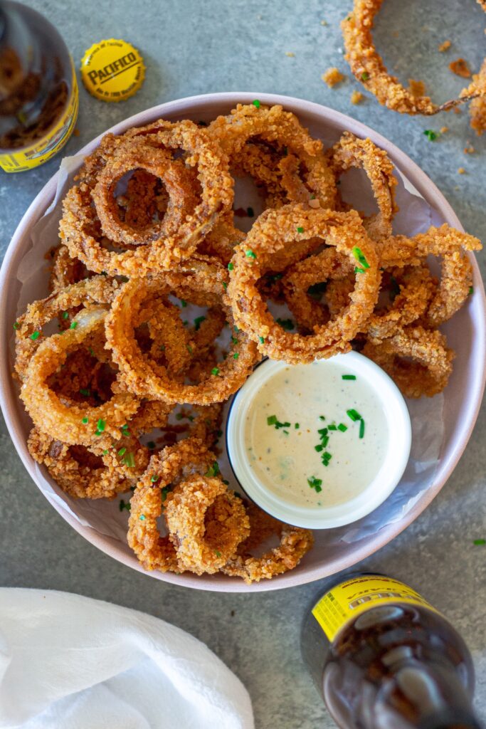 Golden fried onion rings stacked on a plate with a side of white BBQ sauce (aka Alabama sauce) for dipping.