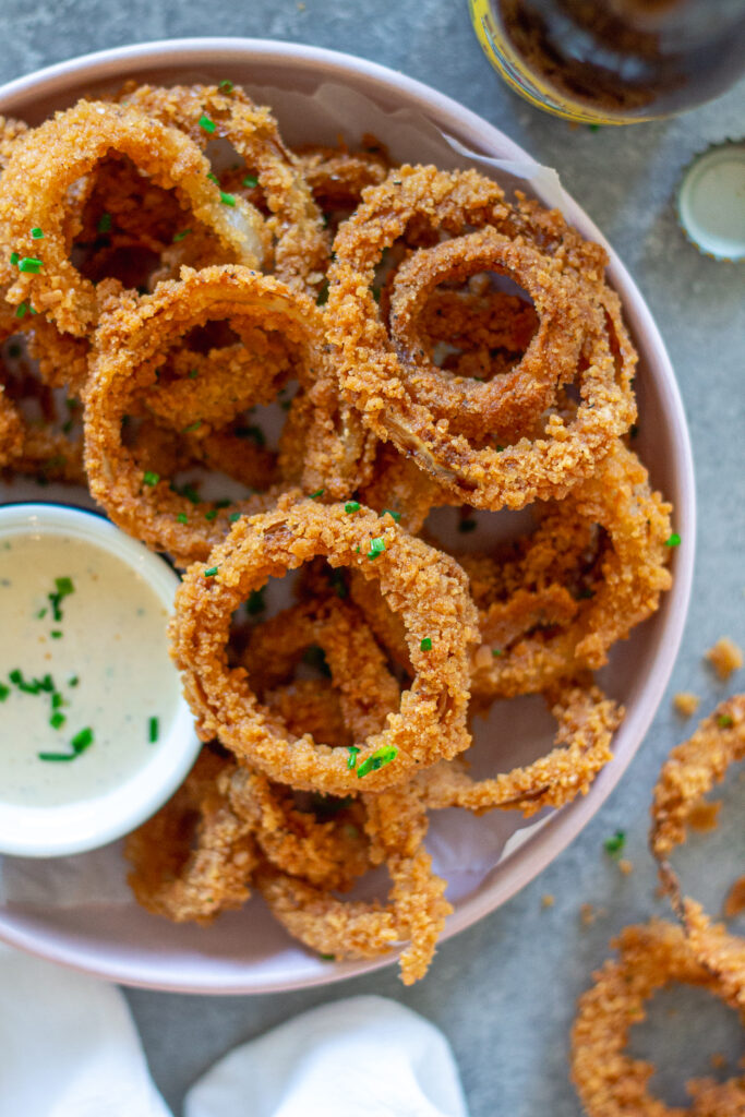 Golden fried onion rings stacked on a plate with a side of white BBQ sauce (aka Alabama sauce) for dipping.