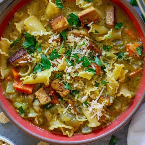 Creamy vegan chicken noodle soup garnished with parsley and parmesan, and served with a side of oyster crackers.