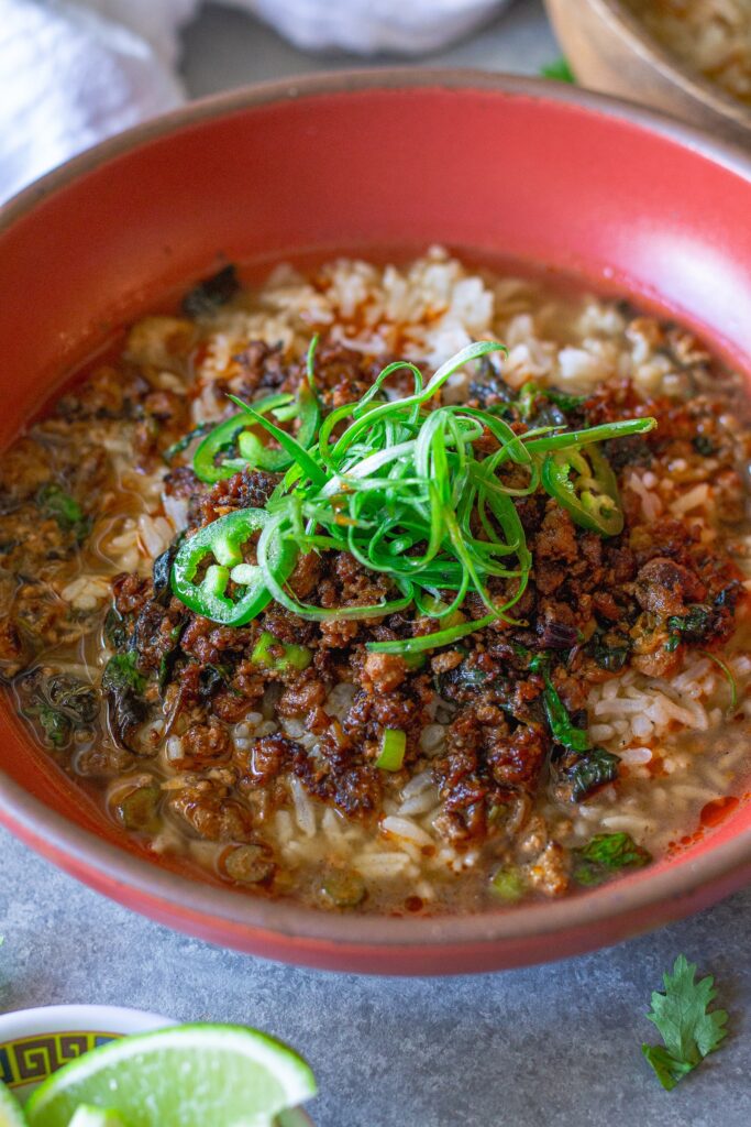 A cozy bowl of crispy cumin-spiced tofu over white rice with broth poured on top, garnished with green onion.