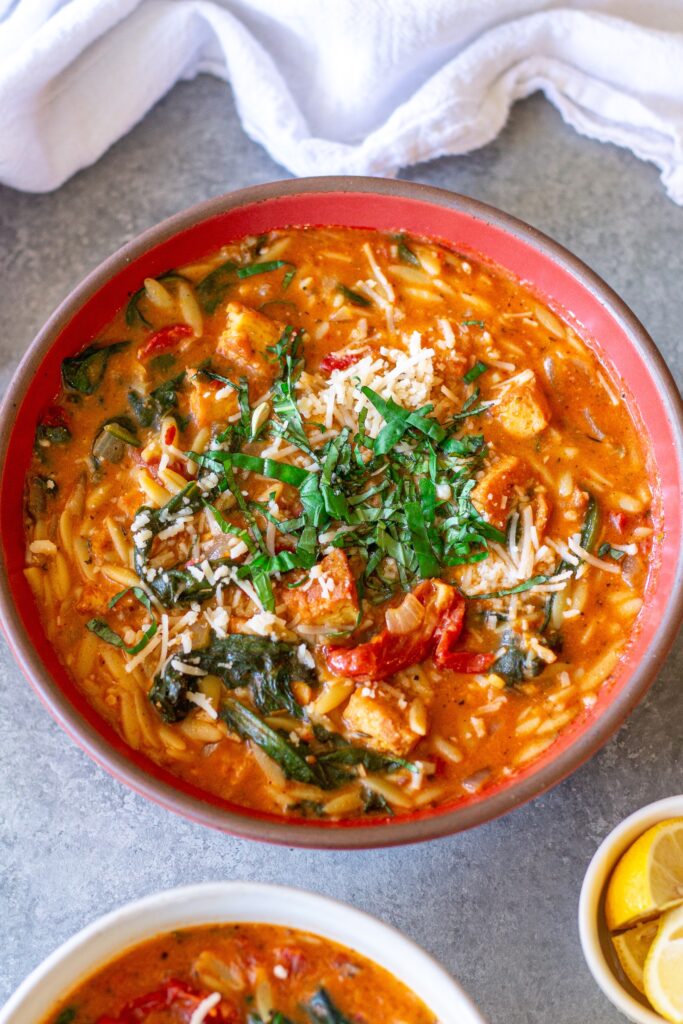 creamy bowl of Vegan Marry Me “Chicken” and Orzo Soup with crispy tofu, spinach, and garnished with parmesan and basil.
