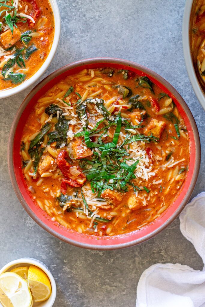 creamy bowl of Vegan Marry Me “Chicken” and Orzo Soup with crispy tofu, spinach, and garnished with parmesan and basil.