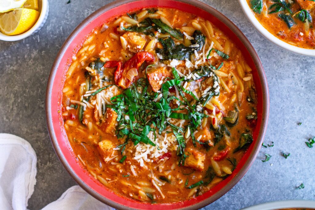 creamy bowl of Vegan Marry Me “Chicken” and Orzo Soup with crispy tofu, spinach, and garnished with parmesan and basil.