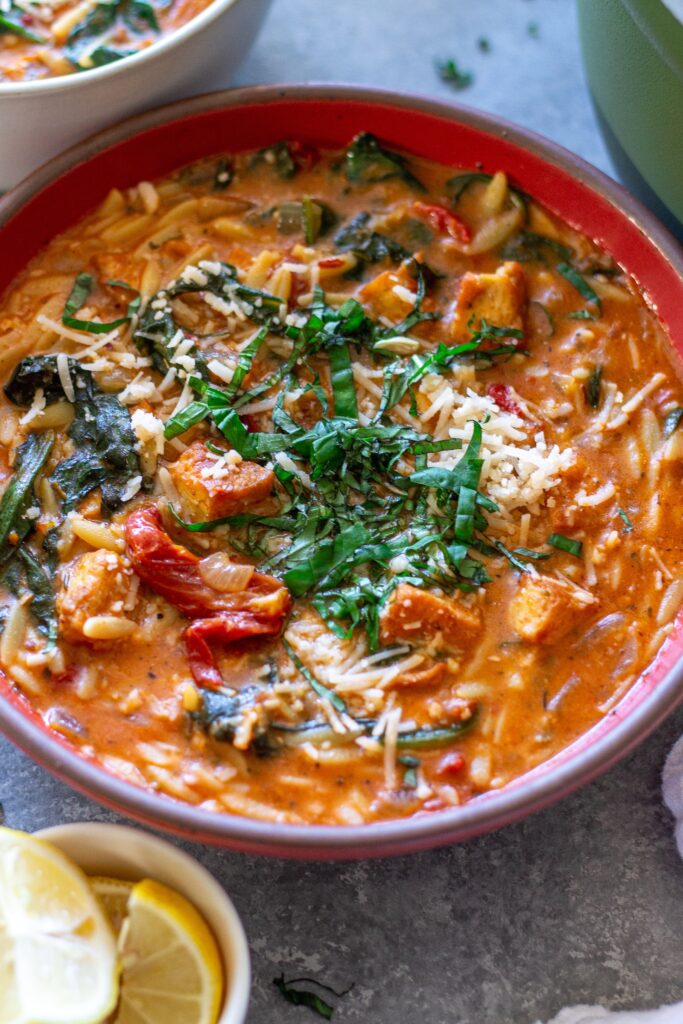 creamy bowl of Vegan Marry Me “Chicken” and Orzo Soup with crispy tofu, spinach, and garnished with parmesan and basil.