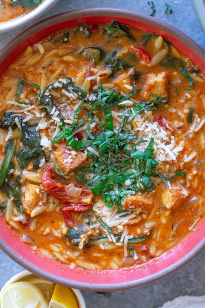 creamy bowl of Vegan Marry Me “Chicken” and Orzo Soup with crispy tofu, spinach, and garnished with parmesan and basil.