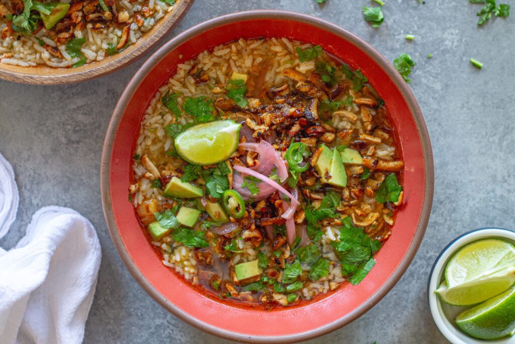 Overhead bowl of chipotle-spiced tofu and cilantro-lime brothy rice topped with pickled onion, avocado, cilantro, and jalapeño slices.