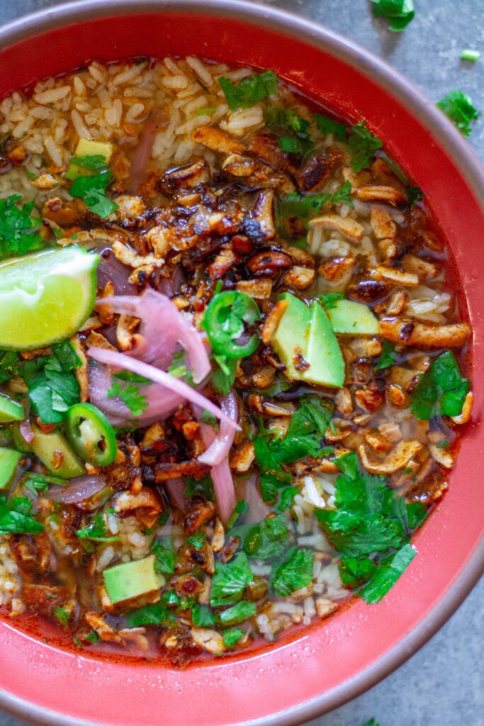 Overhead bowl of chipotle-spiced tofu and cilantro-lime brothy rice topped with pickled onion, avocado, cilantro, and jalapeño slices.