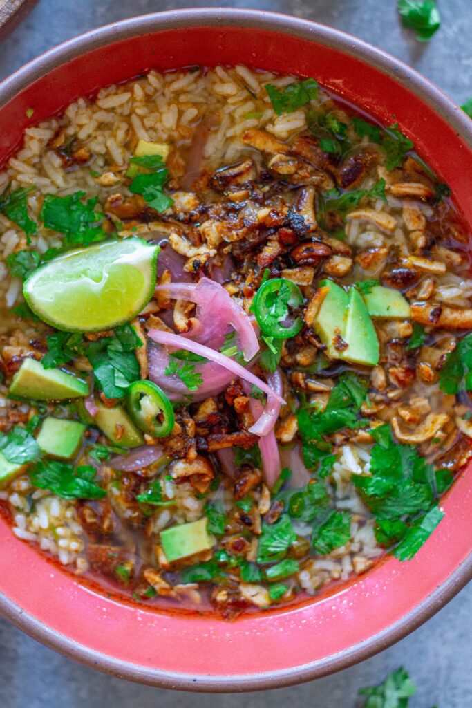 Overhead bowl of chipotle-spiced tofu and cilantro-lime brothy rice topped with pickled onion, avocado, cilantro, and jalapeño slices.