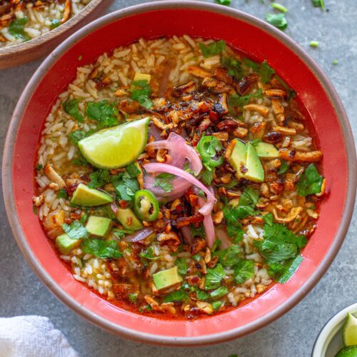 Overhead bowl of chipotle-spiced tofu and cilantro-lime brothy rice topped with pickled onion, avocado, cilantro, and jalapeño slices.
