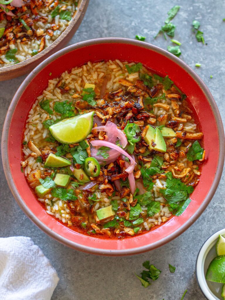 Overhead bowl of chipotle-spiced tofu and cilantro-lime brothy rice topped with pickled onion, avocado, cilantro, and jalapeño slices.