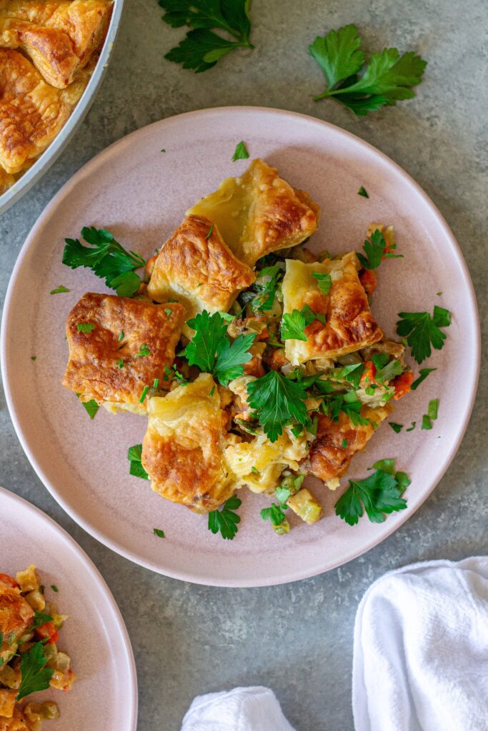 Overhead shot of vegan tofu pot pie with creamy veggie filling, topped with golden and flaky puff pastry squares, then garnished with fresh parsley.