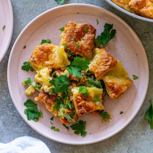 Overhead shot of vegan tofu pot pie with creamy veggie filling, topped with golden and flaky puff pastry squares, then garnished with fresh parsley.